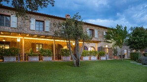 A stone building with a covered patio, outdoor seating, and a well-maintained lawn. - Agriturismo Podere l'Aione (Scansano)