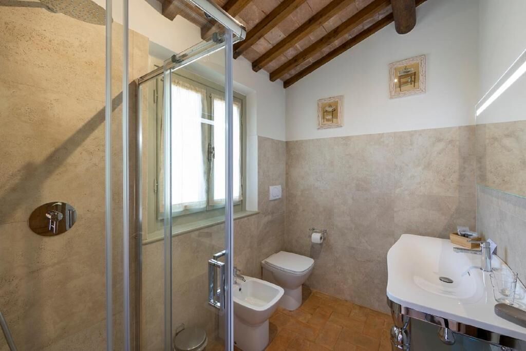 A bathroom with a glass shower enclosure, a toilet, and a sink with a mirror.