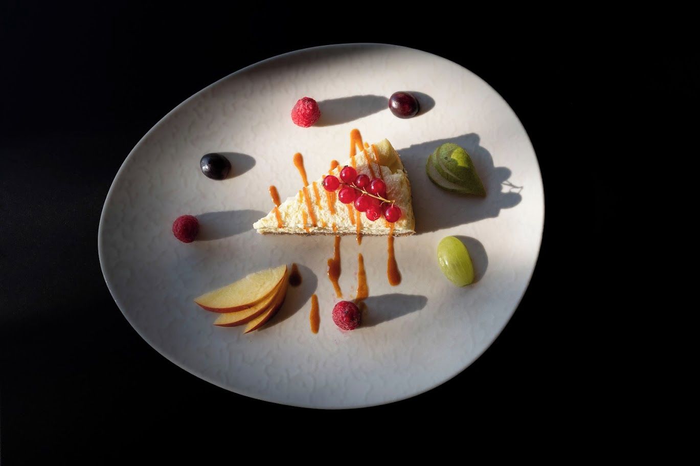 A dessert plate with a slice of cake, fruit, and sauce.