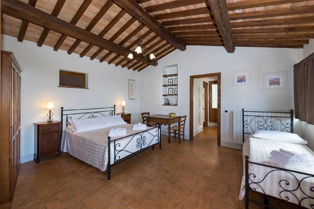 Un dormitorio con dos camas, techo de madera, una mesita y una silla.