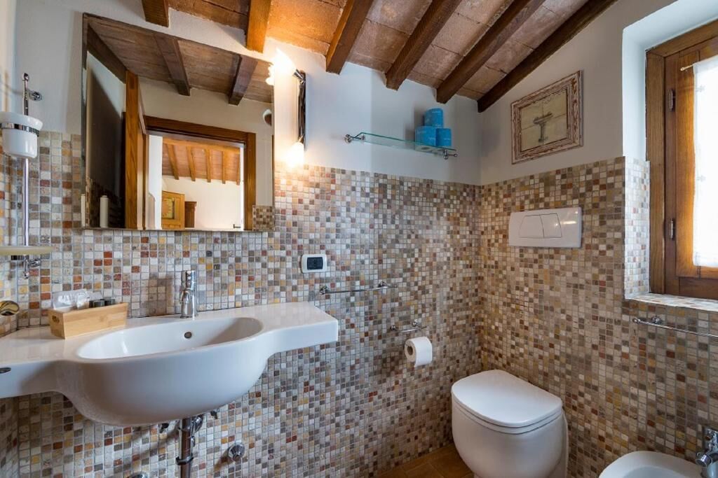 A bathroom with a mosaic tile backsplash, a white sink, a toilet, and a mirror.