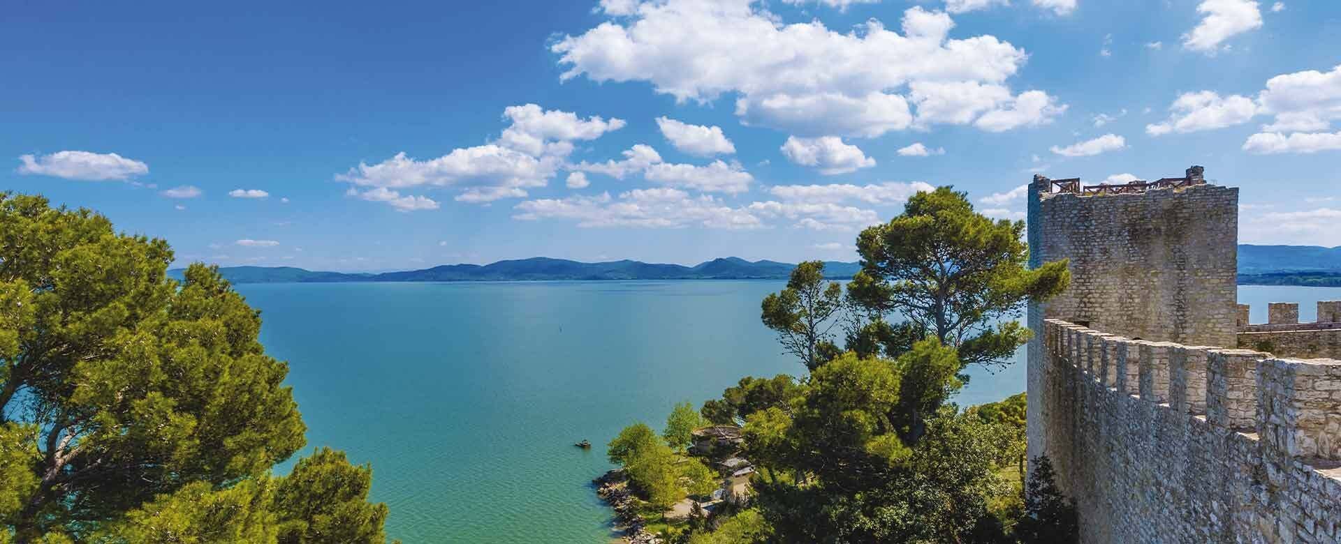 A historic stone tower overlooking a calm lake with distant mountains and clear skies.