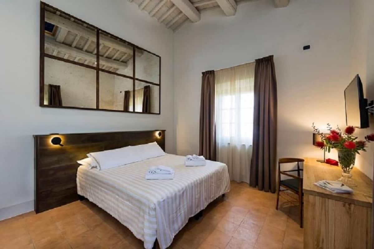 Een hotelkamer met een groot bed, een bureau met stoel, een spiegel en een raam met gordijnen.