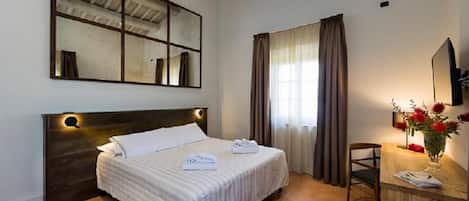 A hotel room with a large bed, a desk with a chair, a mirror, and a window with curtains.