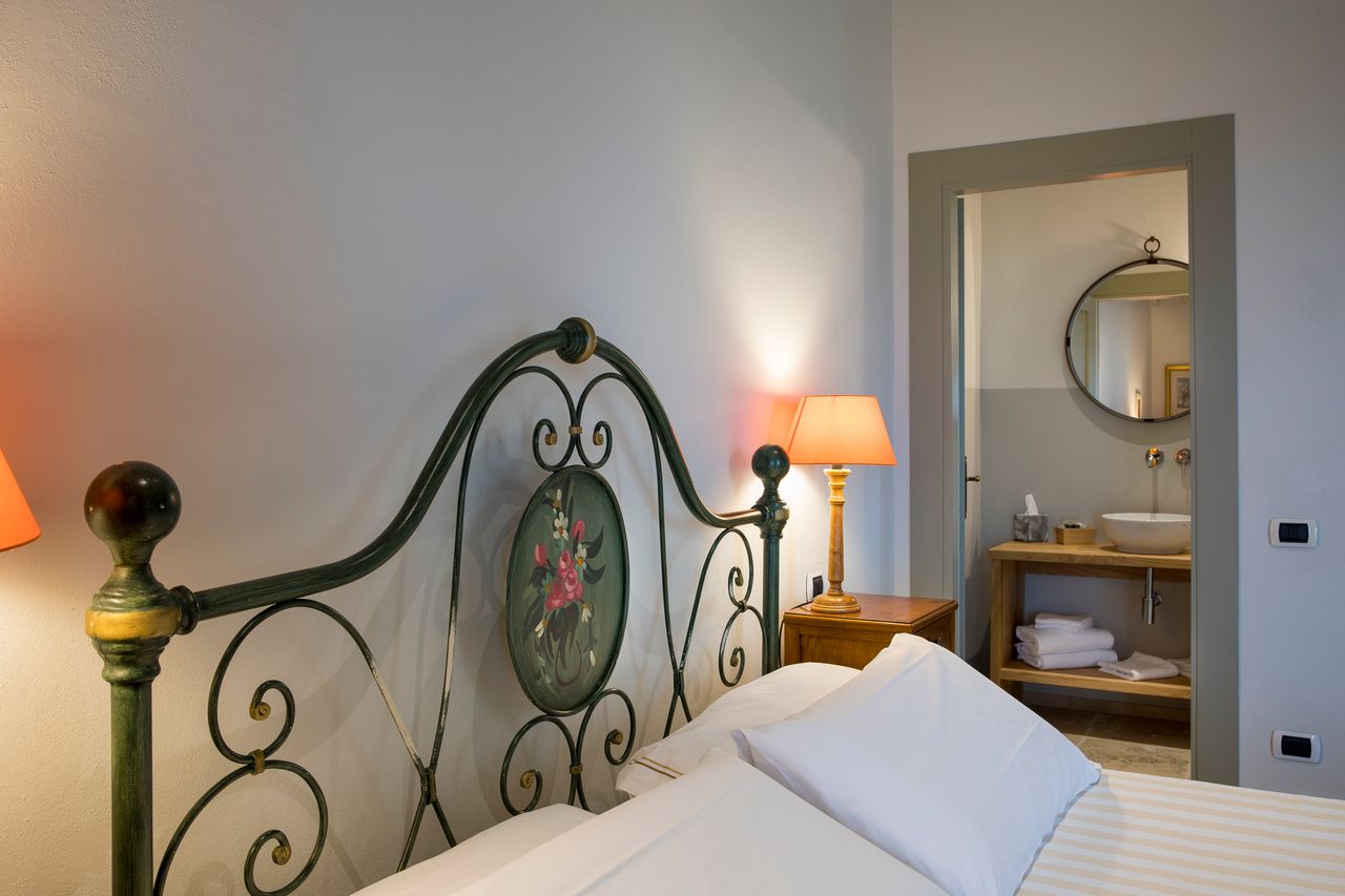 A neatly made bed with a headboard, a bedside lamp, and a wall-mounted mirror.