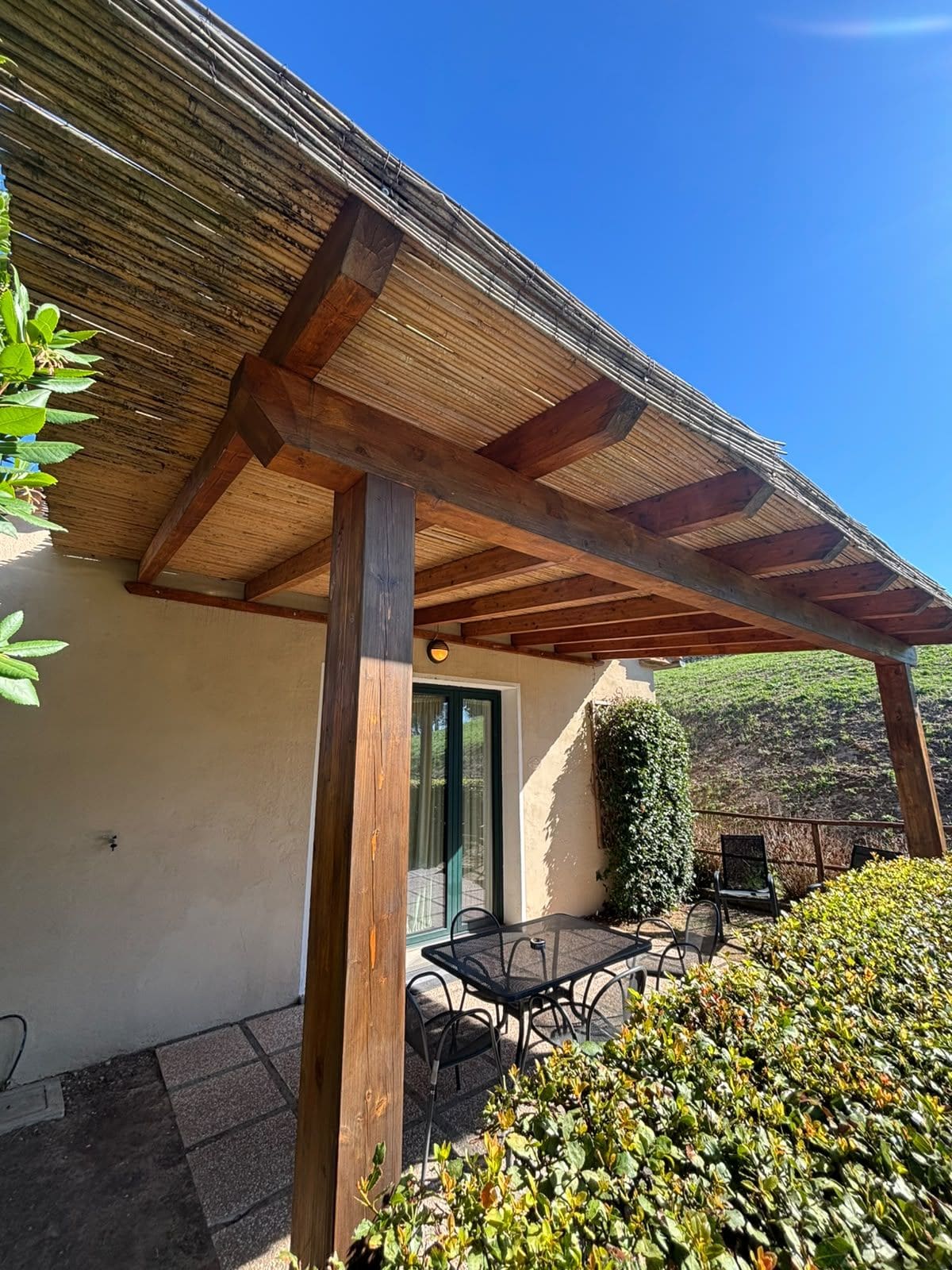 Ein überdachter Patio-Bereich mit einer Holzw pergola, Sitzgelegenheiten im Freien und Blick auf einen angelegten Garten.