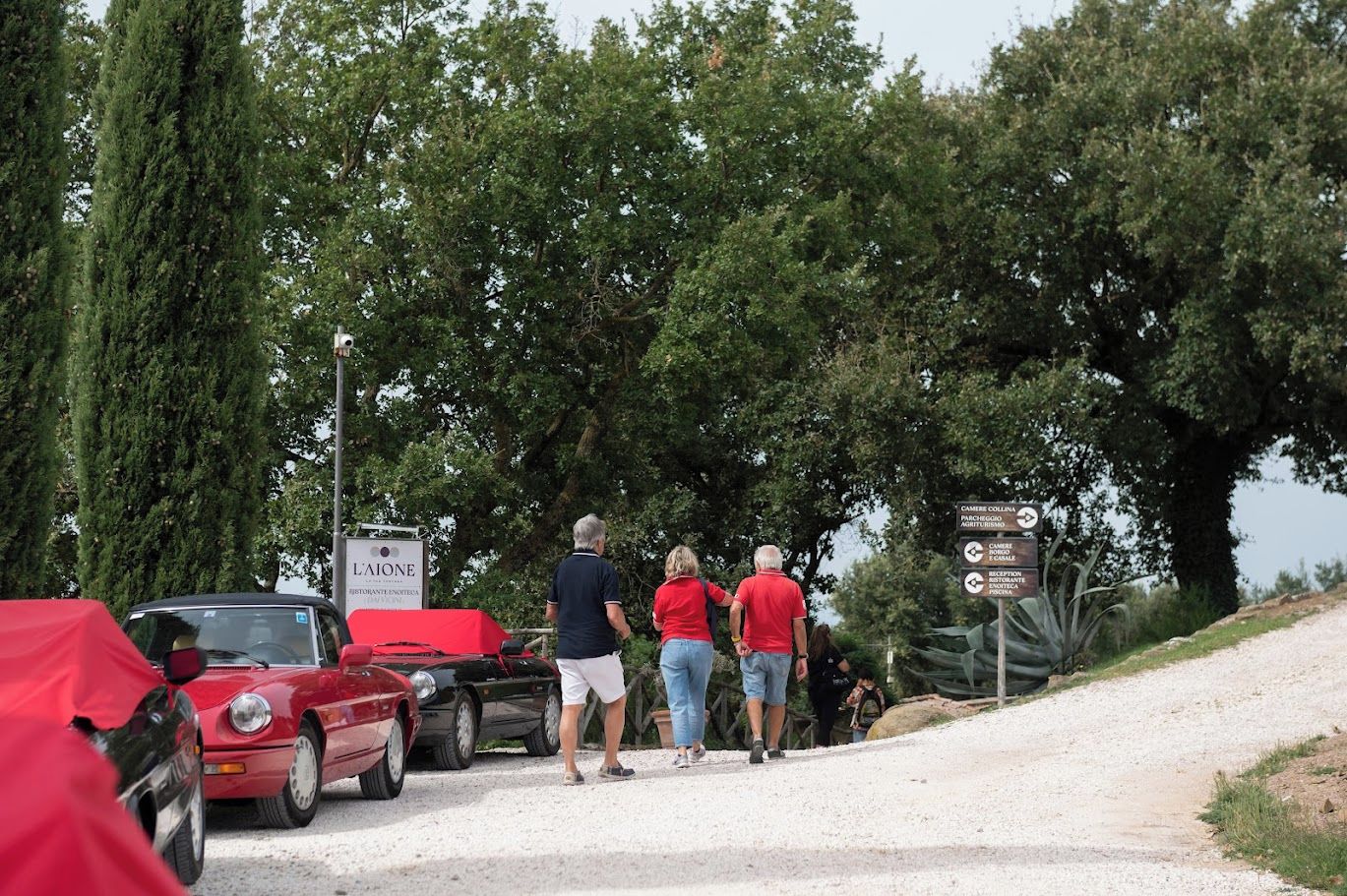 A gravel path leading to a parking area with parked cars and a signpost indicating directions to various facilities.