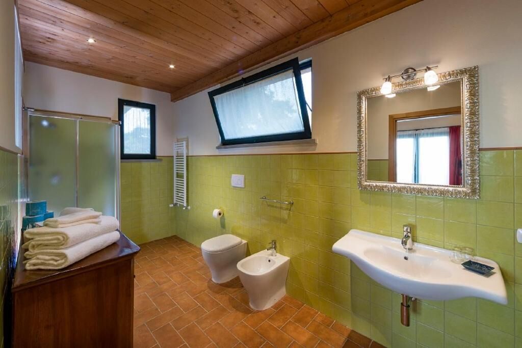 A bathroom with a wooden ceiling, a large mirror, a sink, a bidet, and a window.