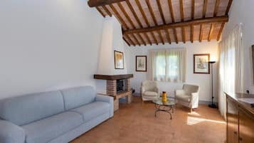 Un soggiorno con divano, due poltrone, tavolino, camino e soffitto in legno.