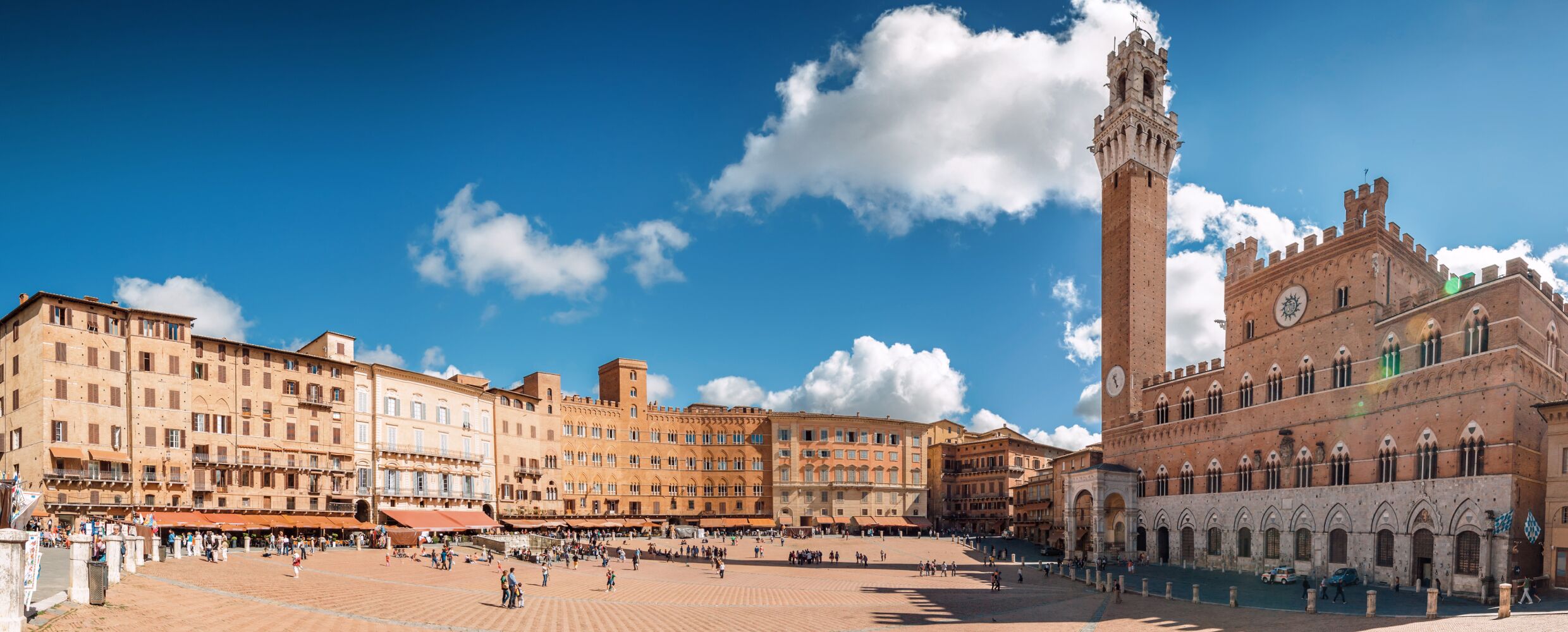 A spacious public square with historic buildings, a prominent clock tower, and a clear blue sky.