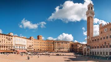 A spacious public square with historic buildings, a prominent clock tower, and a clear blue sky.