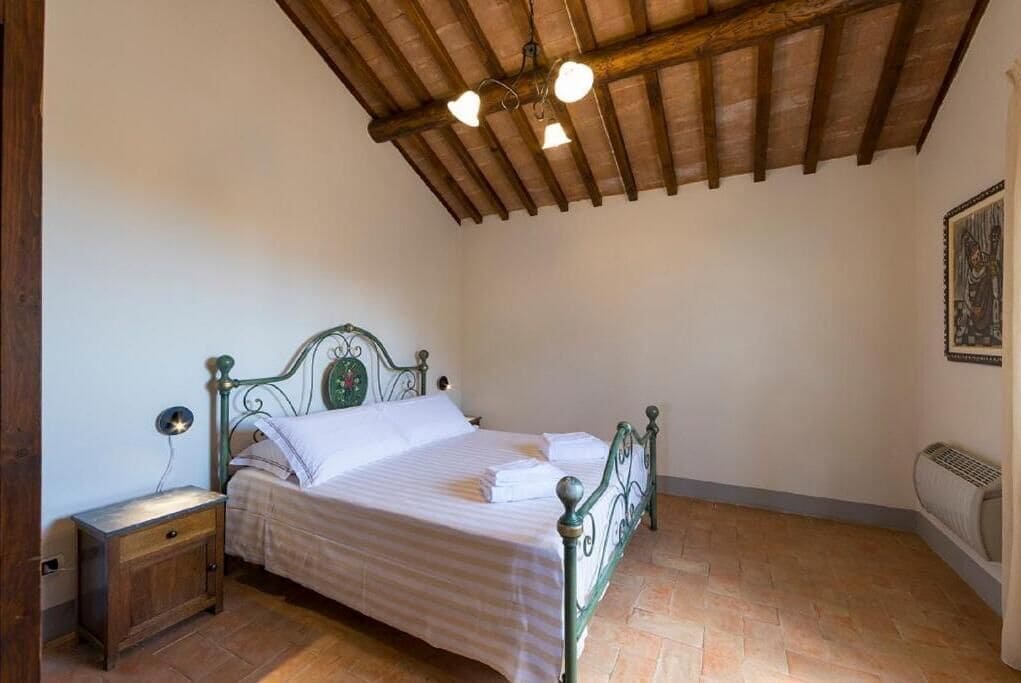 Ein Schlafzimmer mit Holzboden, einem Bett mit Metallgestell, einem Nachttisch und einer Heizung.