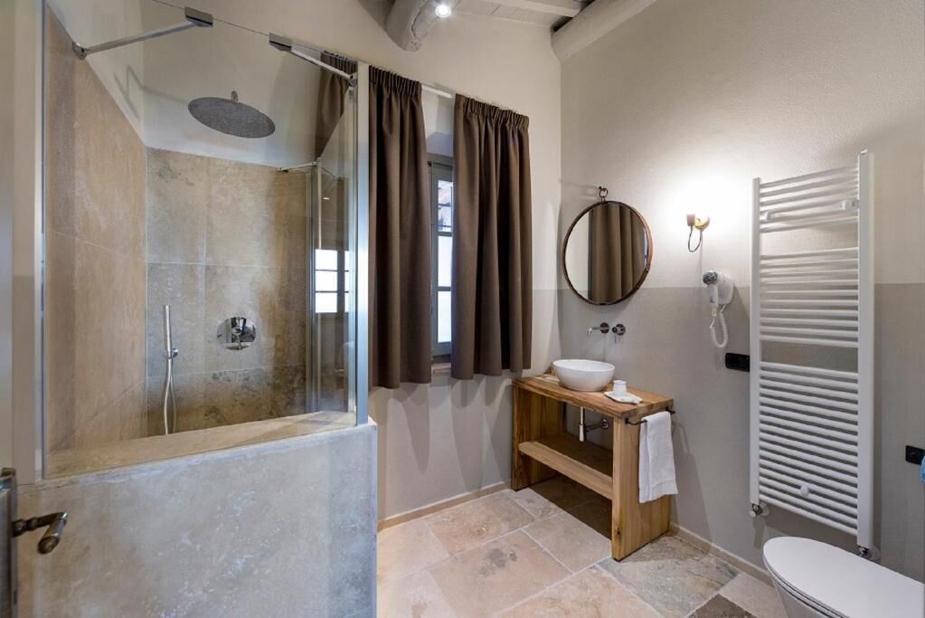 Un baño con ducha envuelta en vidrio, un tocador de madera con lavabo, un inodoro y un perchero para toallas.