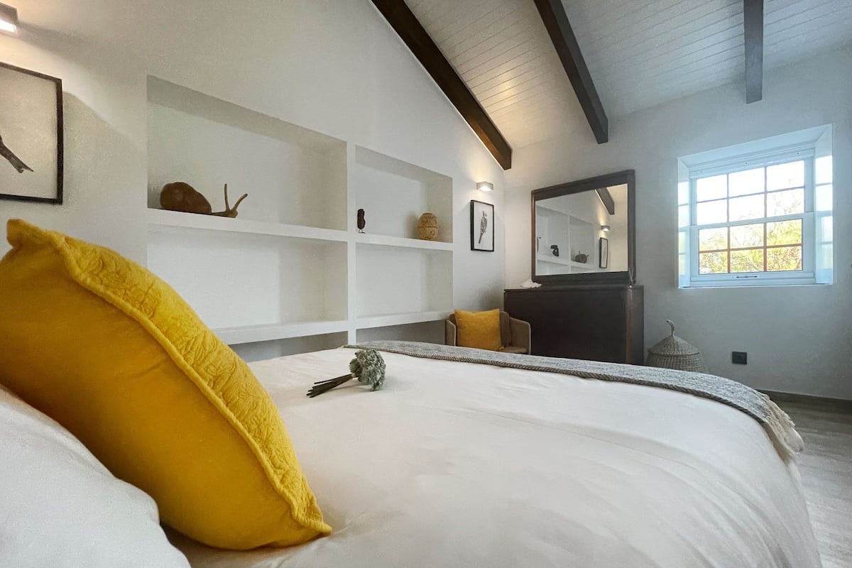 Un dormitorio con cama, ventana, espejo y estanterías empotradas.