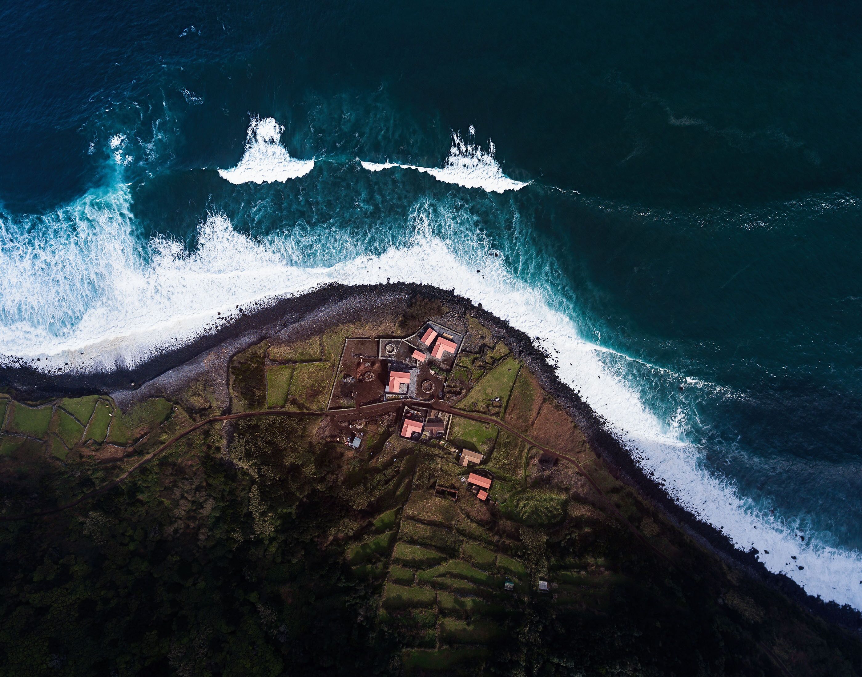 An aerial view of a coastal village with houses along the shoreline, surrounded by waves.