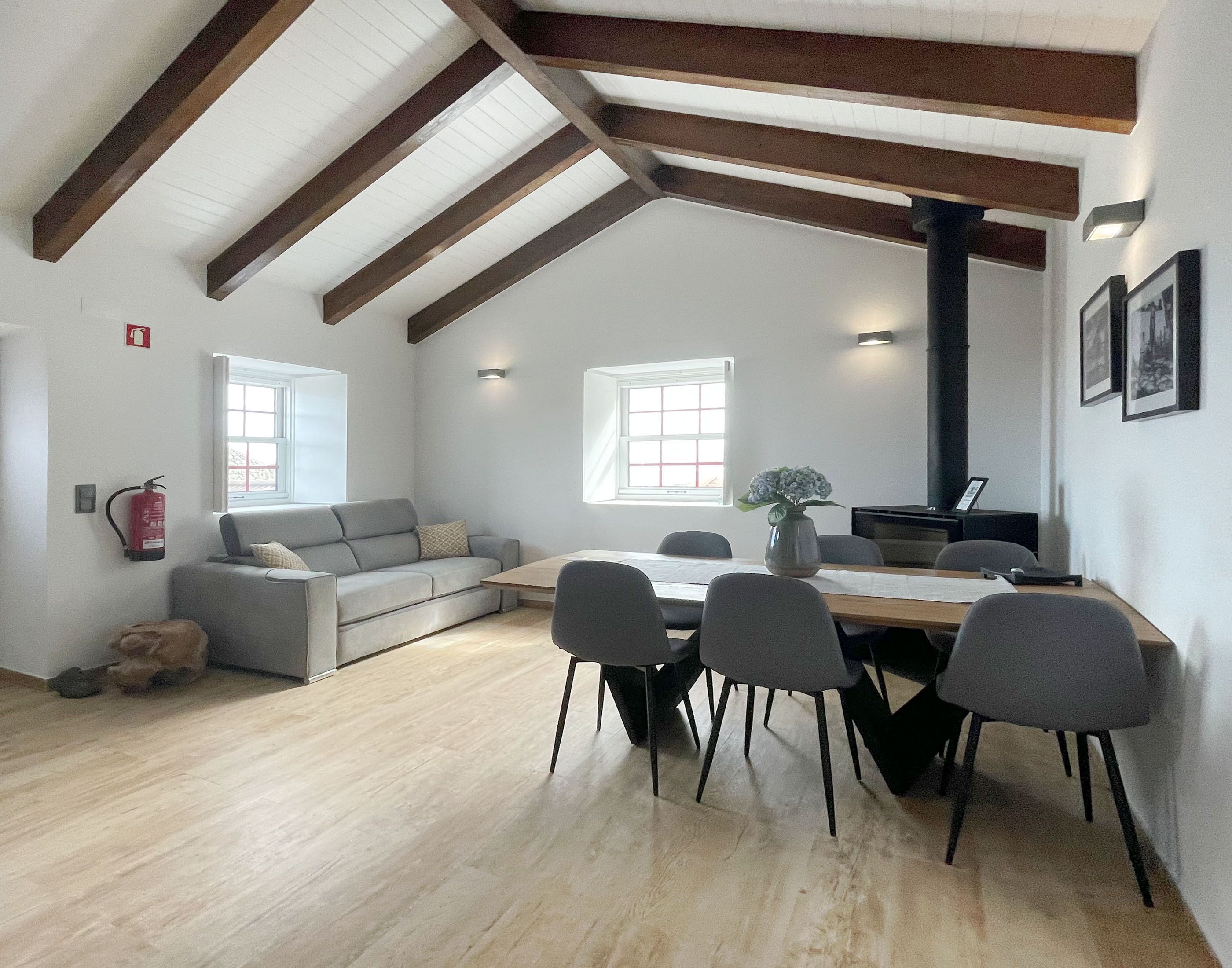 A spacious loft with exposed wooden beams, a dining area with a table and chairs, a sofa, and a fireplace.