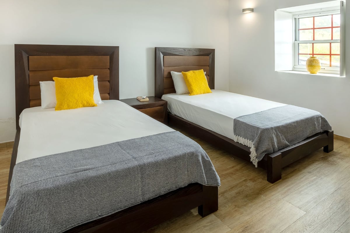 Dos camas con cabeceras de madera, sábanas blancas y almohadas amarillas.