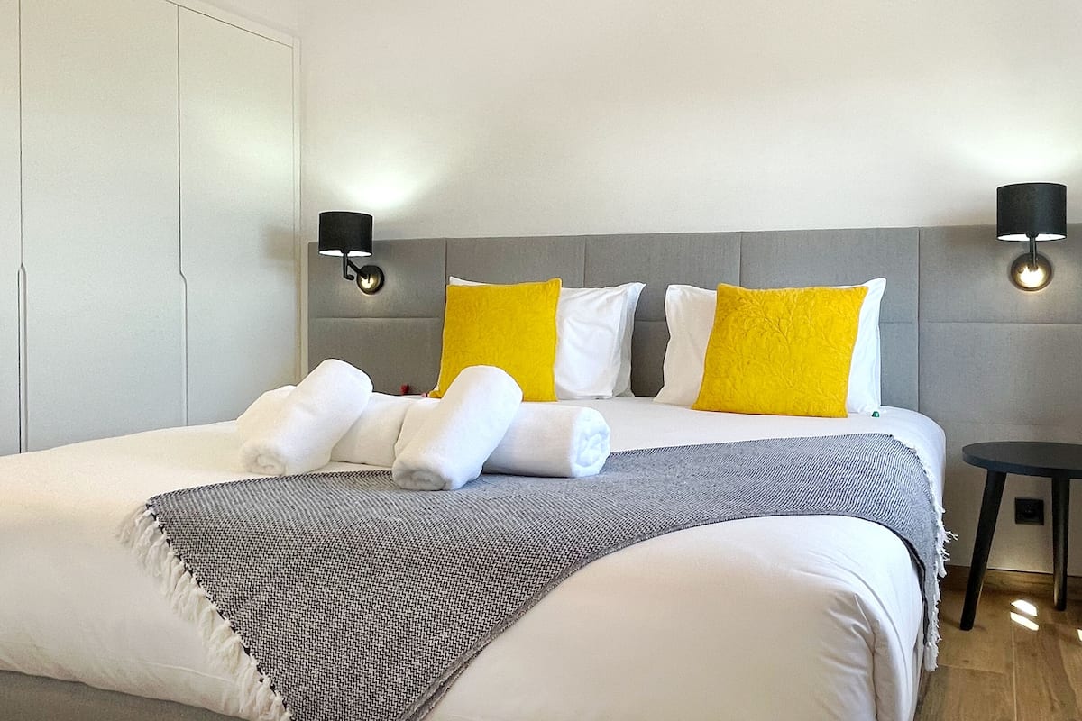 Una habitación de hotel con una cama grande, dos lámparas de noche y una mesita pequeña.