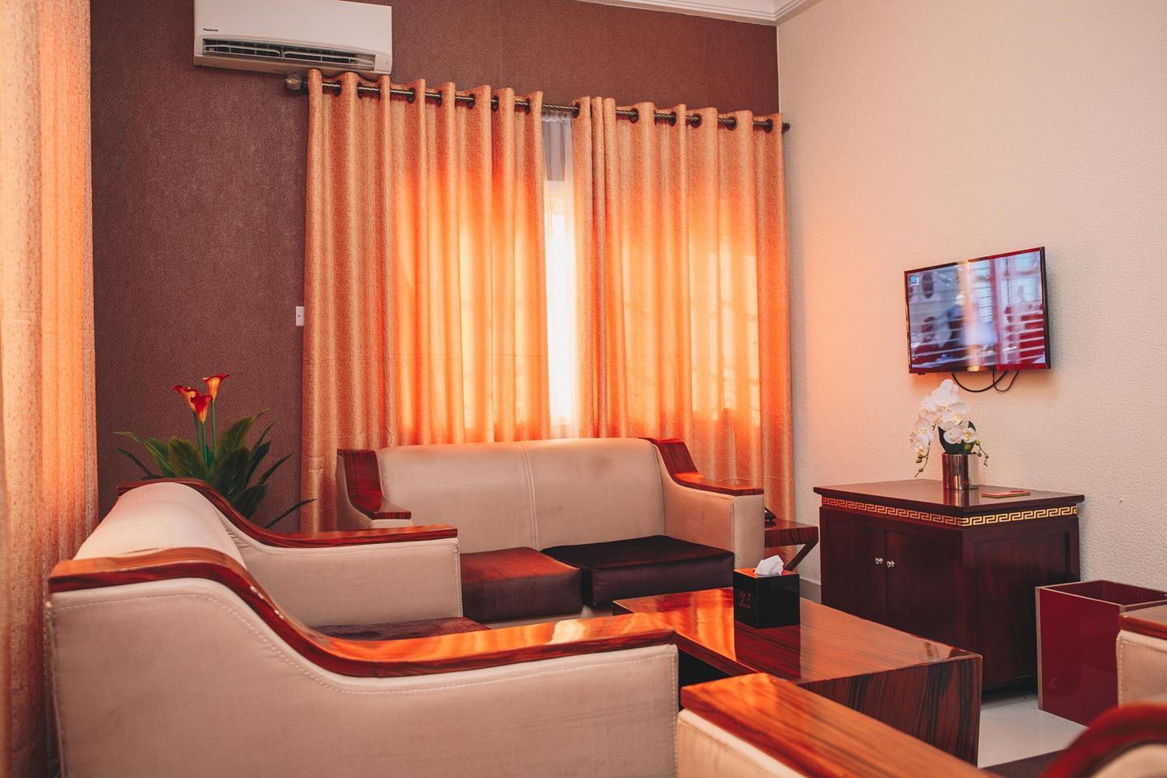 A hotel room with a sofa, armchairs, a wooden coffee table, a small desk, and a TV mounted on the wall.