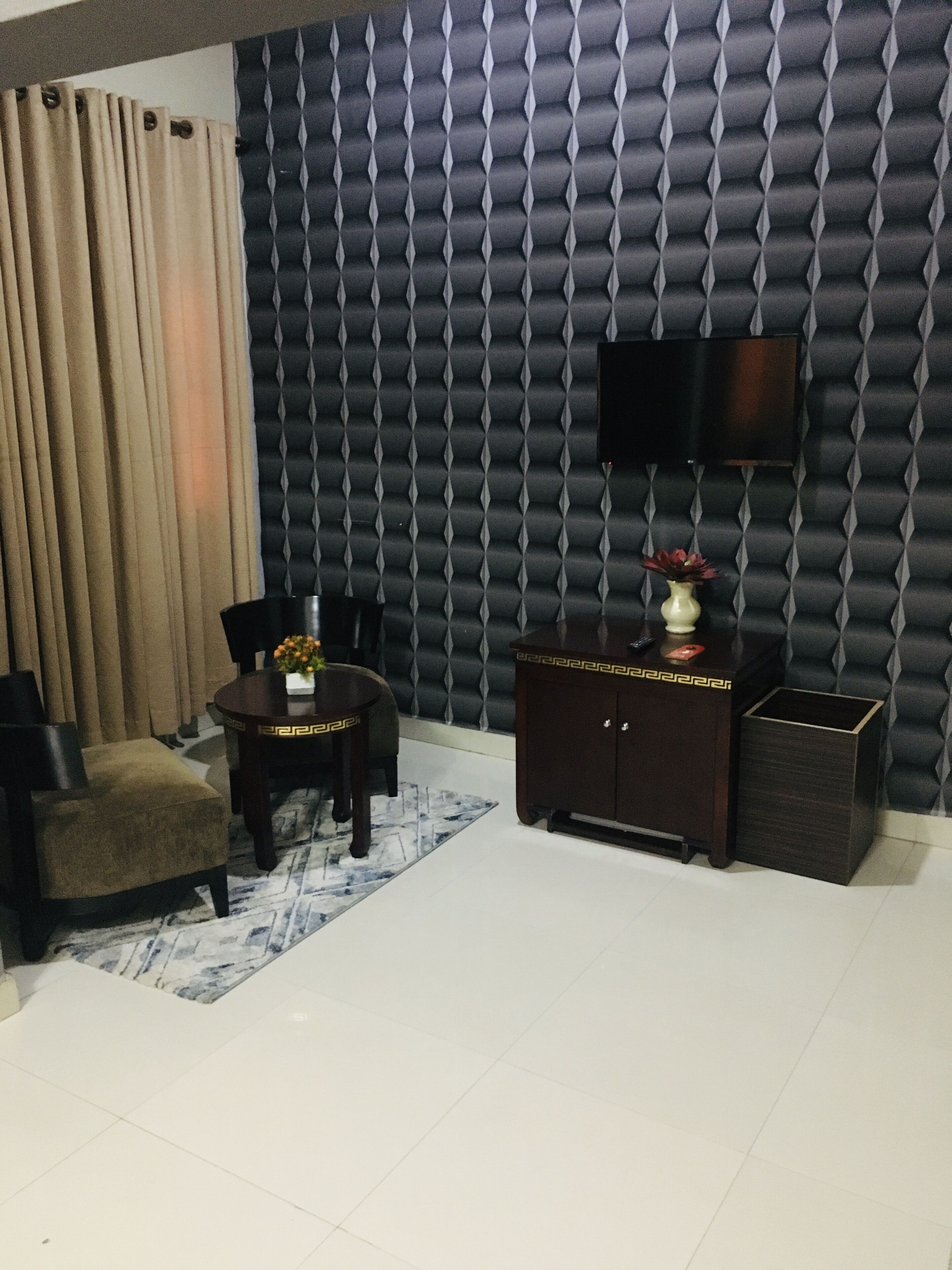 A living room with a sofa, a coffee table with a vase, a TV mounted on a textured wall, and a trash bin.