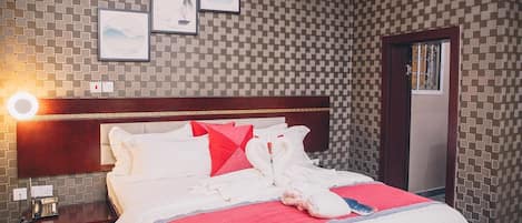 A hotel room with a checkered wall pattern, a wooden headboard, a bed with white bedding and red accents, a bedside table with a phone, and framed pictures on the wall.