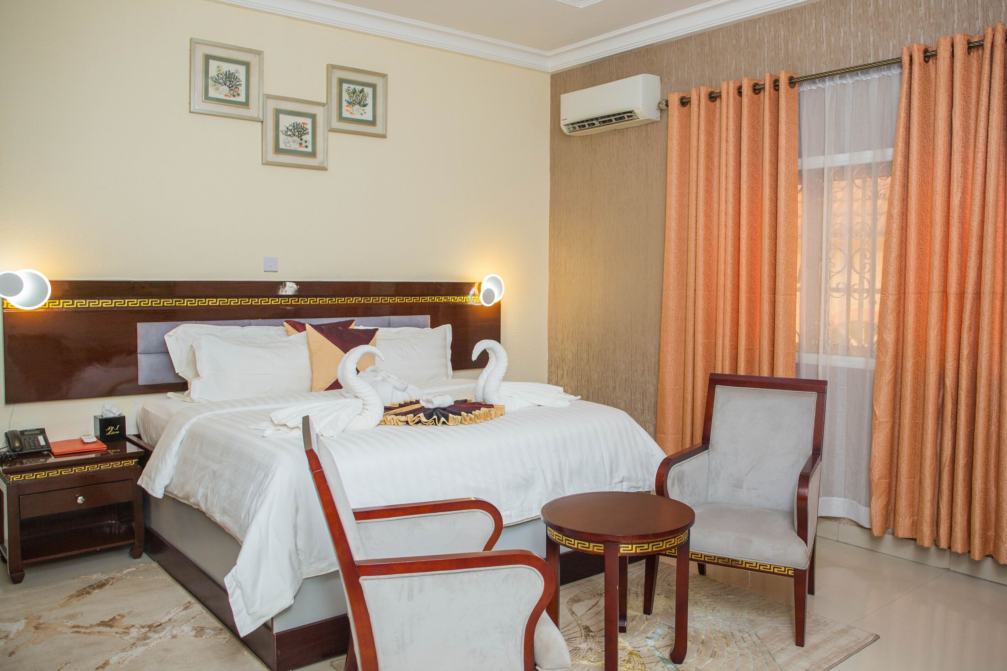 A hotel room with a large bed, two chairs, a small table, a nightstand, and wall-mounted air conditioning.