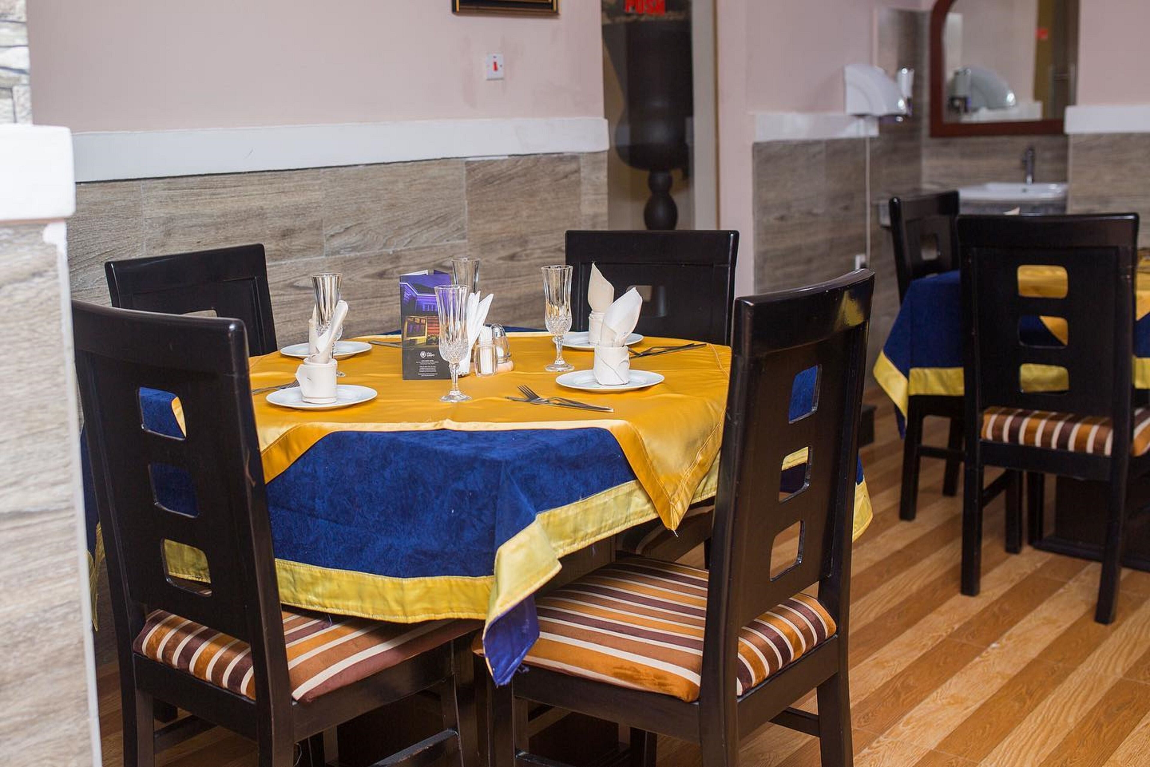 A dining area with a table set for four, featuring a yellow tablecloth, blue napkins, and white plates.