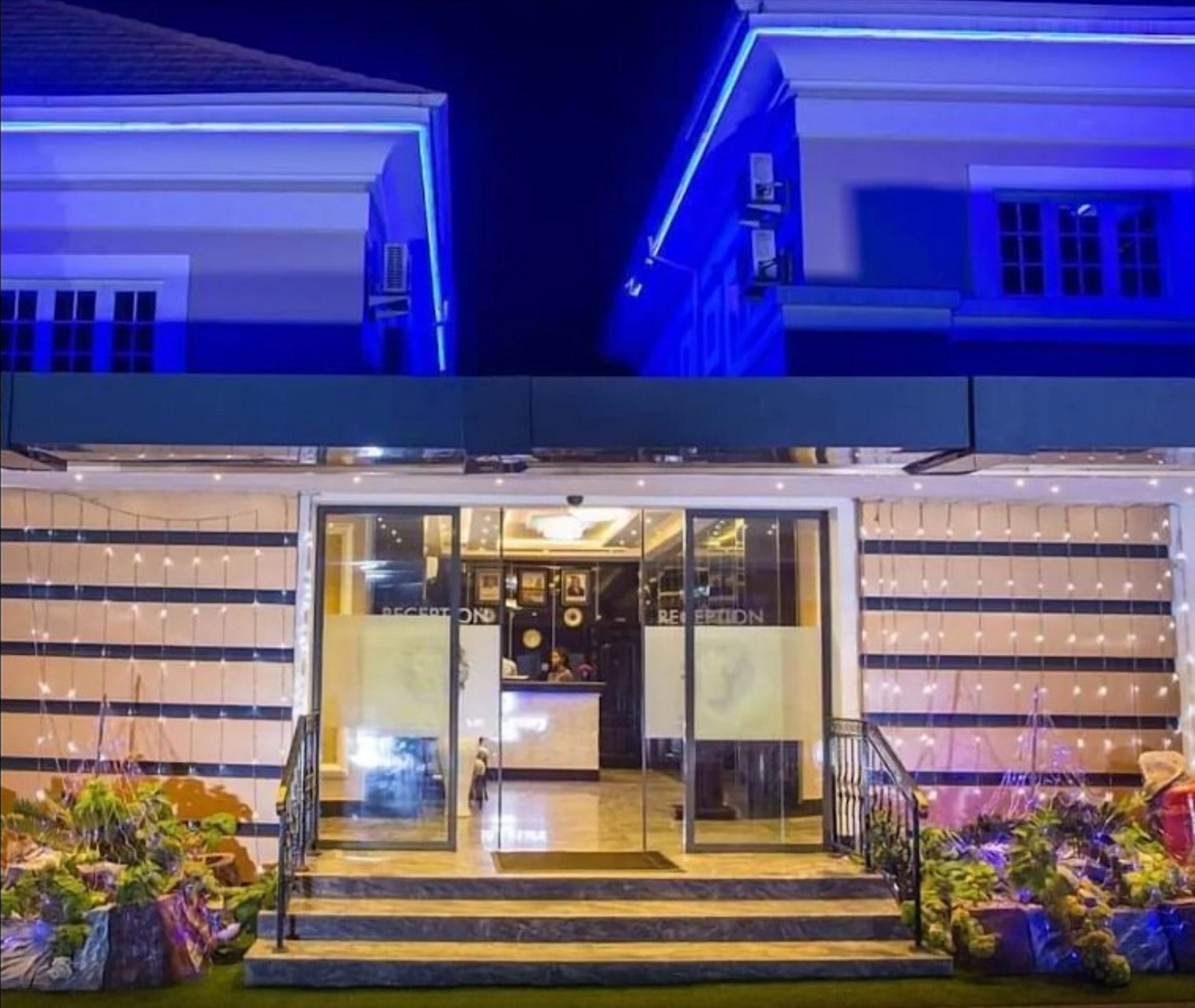 A hotel entrance with a reception desk, glass doors, and a staircase leading up.