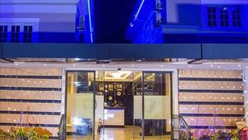 A hotel entrance with a reception desk, glass doors, and a staircase leading up.
