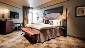 A hotel room with a large bed, a desk, a bench, and a wardrobe.