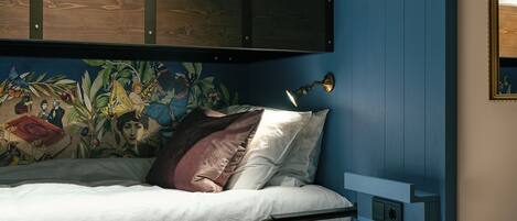 Una cama litera con un mural en la pared, una lámpara de noche y una pequeña estantería.
