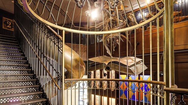 A spiral staircase with ornate metal railings and a golden, spherical sculpture at the top.