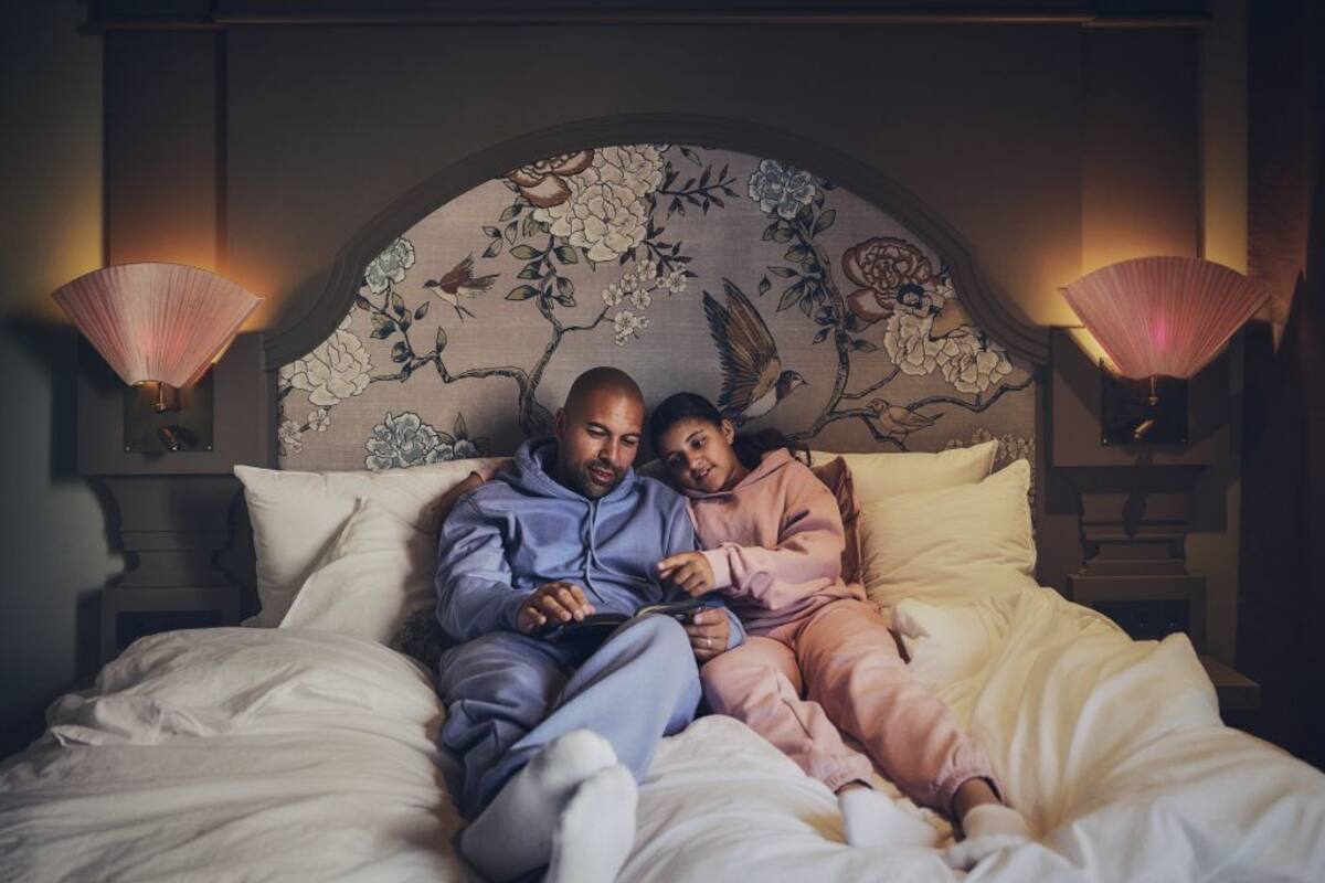 Un couple est allongé sur un lit doté d’une tête de lit à motifs floraux, avec deux lampes de chevet et une table de chevet sur laquelle se trouve une lampe.
