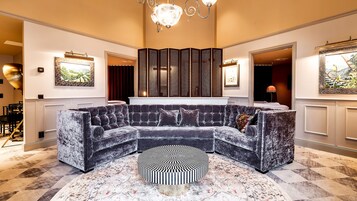 Una lujosa sala de estar con un sofá seccional de terciopelo oscuro, un otomán estampado y un biombo decorativo.