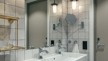 Un baño moderno con un lavamanos grande y blanco, dos espejos, un toallero dorado y una lámpara de pared.
