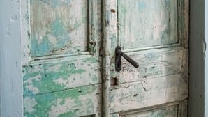 Une porte usée par les intempéries, dont la peinture s’écaillait, avec un loquet bien visible et une petite fenêtre rectangulaire.