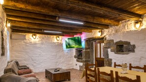 Une pièce rustique avec des murs en pierre, des poutres en bois au plafond, une cheminée en pierre et un téléviseur fixé au mur.