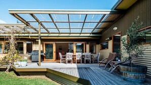 Un patio couvert avec une terrasse en bois, du mobilier d’extérieur et un barbecue.