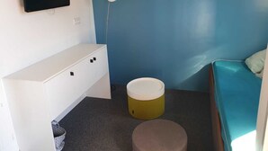 A small, compact room with a blue wall, a white cabinet, a bed with a blue mattress, a small round stool, and a white bucket. - Location LES Arcs 1800 Residence Thuria (LES ARCS 1800)
