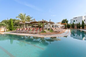 A swimming pool with lounge chairs and umbrellas, surrounded by palm trees and a building. - Playa Ferrera Apartments (Felanitx)