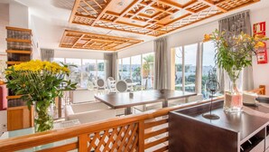 A modern hotel room with a wooden ceiling, large windows, a dining area, and a view of the city. - Playa Ferrera Apartments (Felanitx)