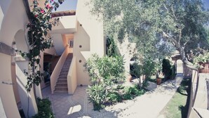 A courtyard with a staircase leading to an upper level, surrounded by greenery and potted plants. - Playa Ferrera Apartments (Felanitx)