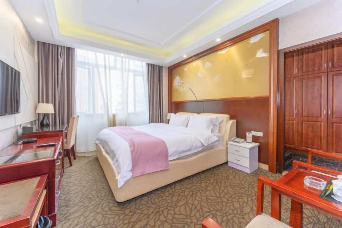 A hotel room with a bed, a desk, a chair, a TV, a bedside table, and a wardrobe.