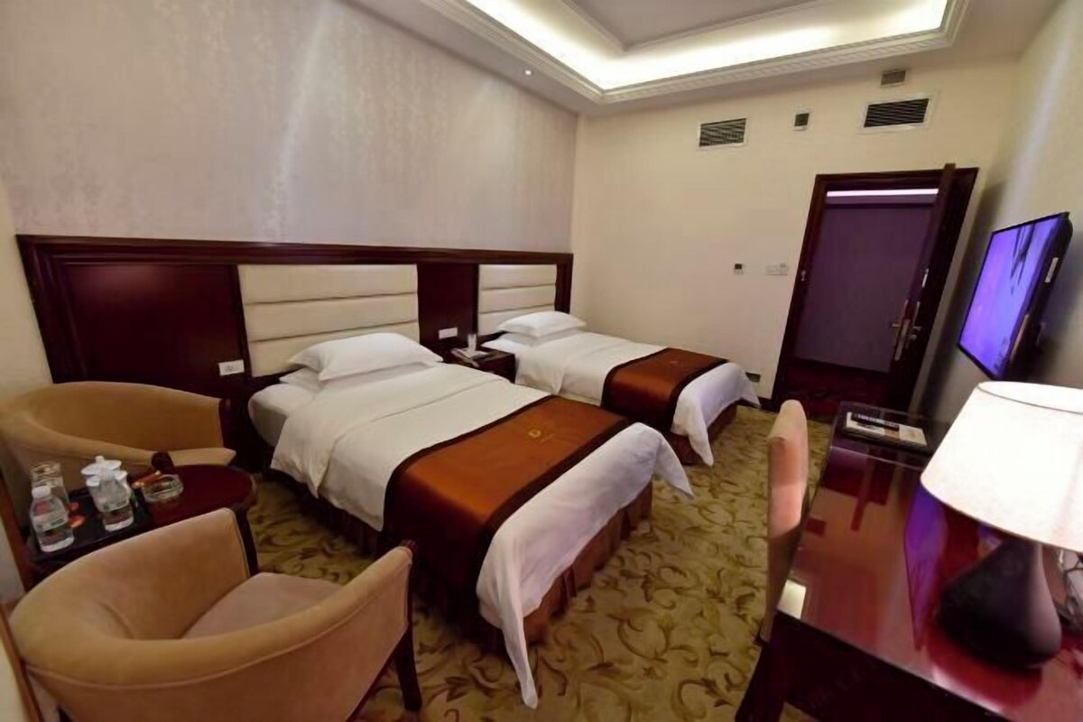 A hotel room with two beds, a desk, a TV, and a chair.