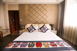 Une chambre d’hôtel avec un grand lit, une tête de lit ornée d’un motif en losanges, deux tables de chevet avec des lampes et une armoire.