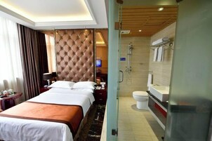 Habitación de hotel con una cama grande, televisión, baño con ducha y mampara de vidrio.