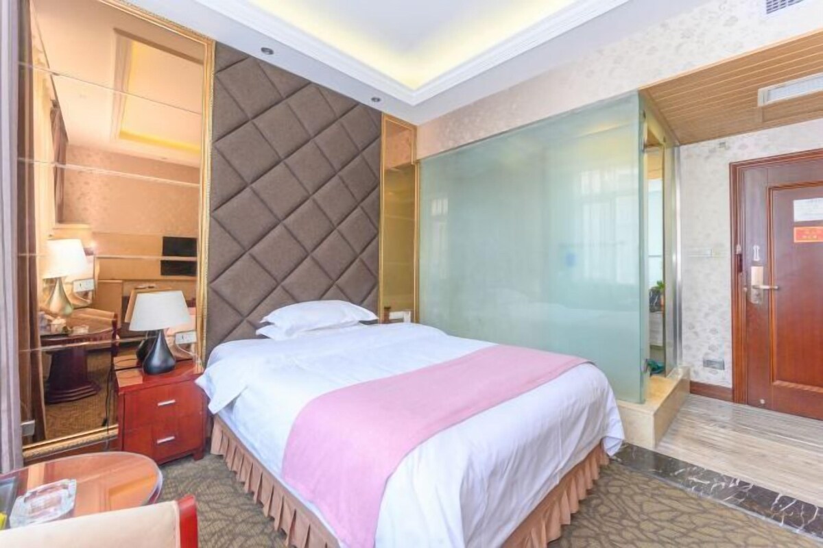 A hotel room with a bed, bedside table, lamp, and a mirror.