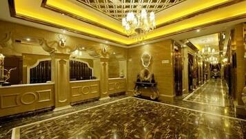 A luxurious hotel lobby with marble flooring, ornate chandeliers, and a grand reception desk.