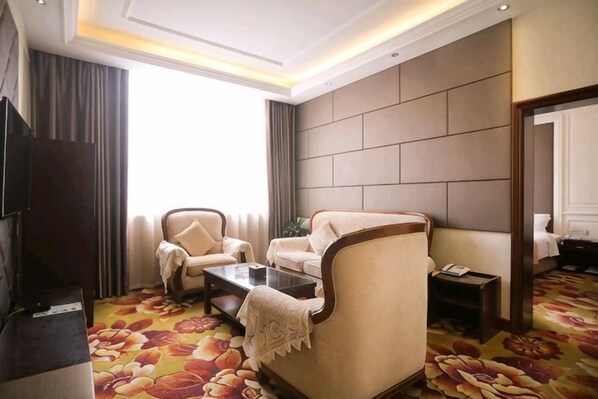 A hotel room with a sofa, armchair, and a television.