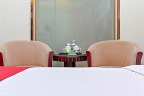 A hotel room with a bed, two chairs, a small table with a water bottle and a cup, and a glass partition. - Donghua Hotel Bazhong (Bazhong)